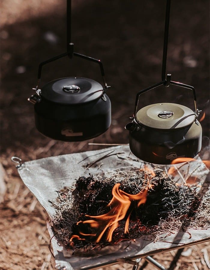 Two camping kettles hanging over a small fire on a fire stand
