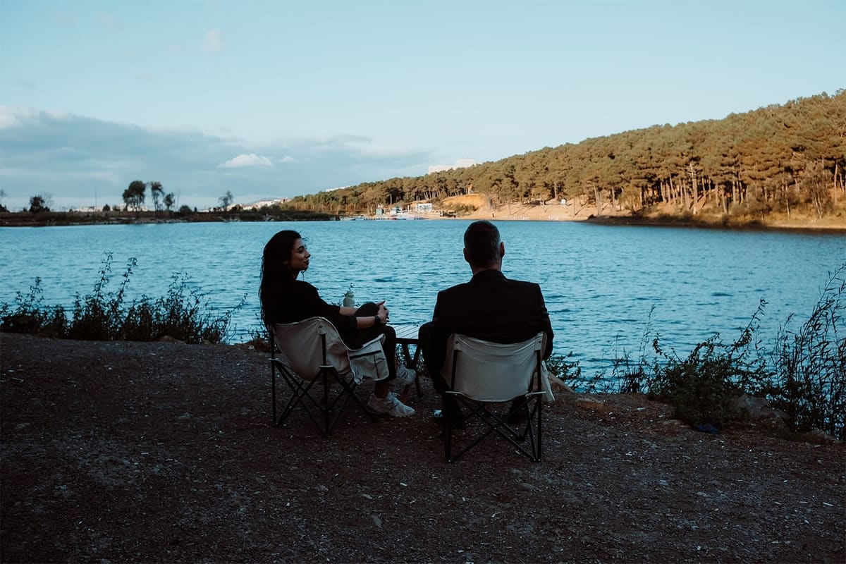 Couple in canvas chairs at a lakeside under a blue sky
