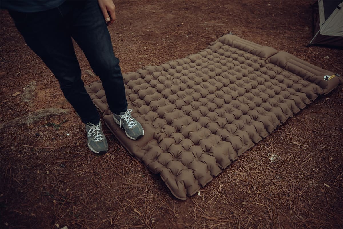Someone stepping onto the Othila double air mattress on a forest floor covered in pine needles