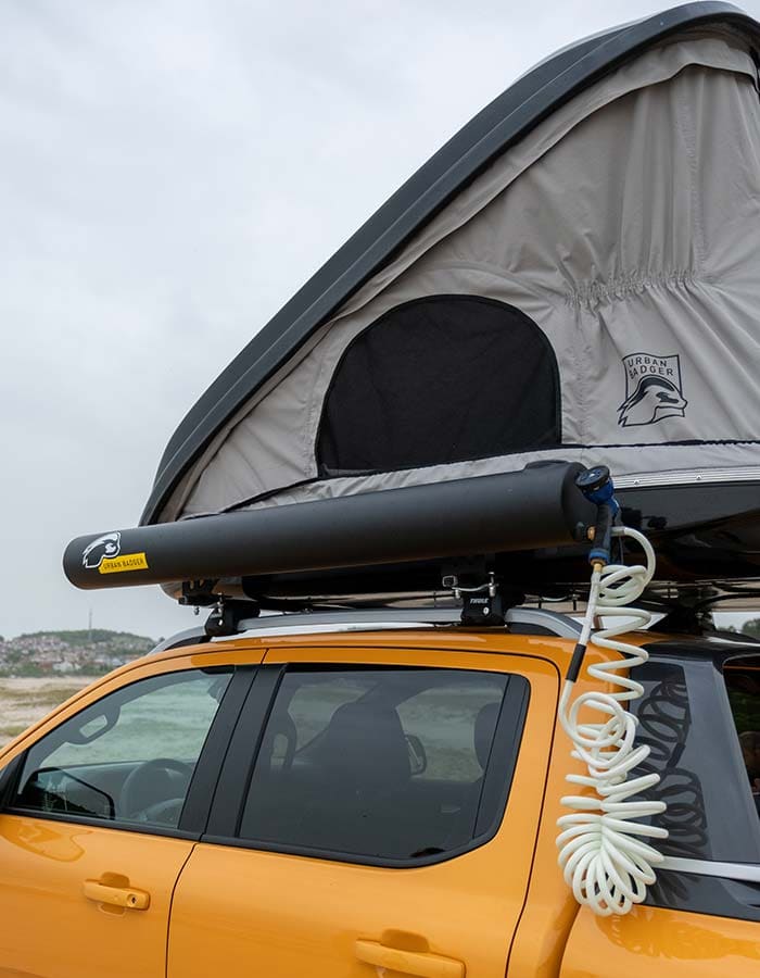 Solar shower tank mounted on the roof rack under the roof top tent, coiled hose hanging down