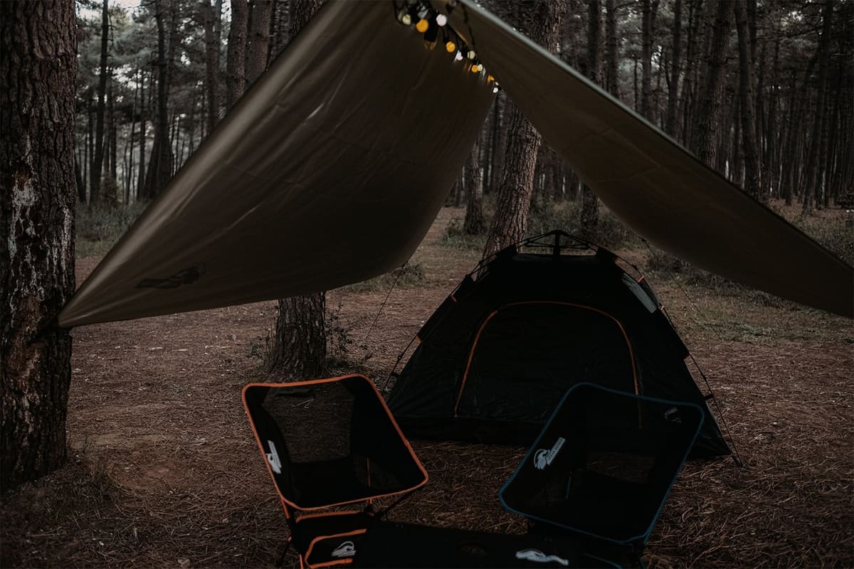 Ragnar tarp tied to a pine over a Midgard tent, two Loki chairs in front and string lights under the ridge