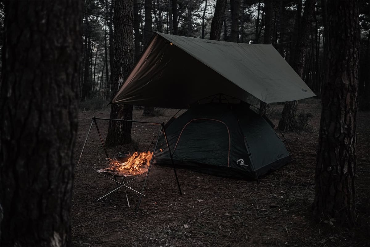 Urban Badger Ragnar tarp over a Midgard tent beside a small campfire in a pine forest at night