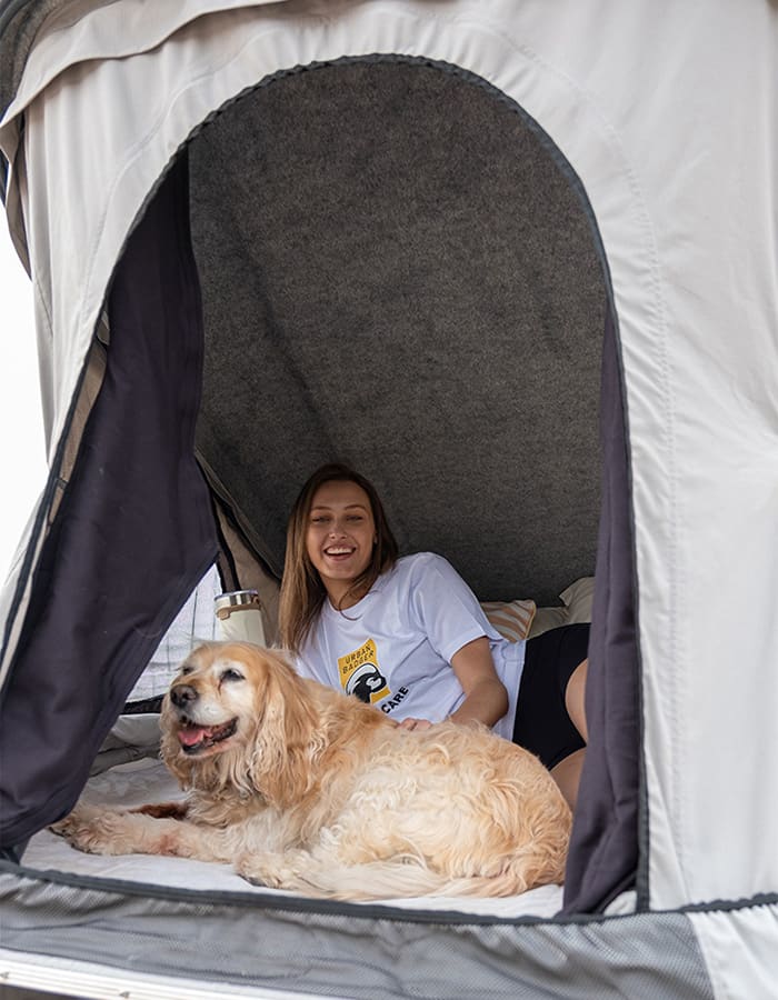 Woman and a golden retriever relaxing on the mattress inside the open roof top tent