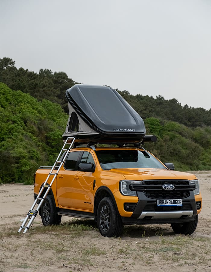 Orange pickup on the beach with the roof top tent on the roof rack and the telescopic ladder leaning against it