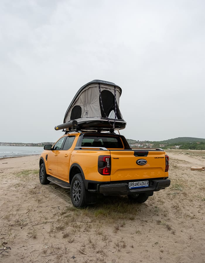 Orange pickup on the sand with the roof top tent open, seen from the rear