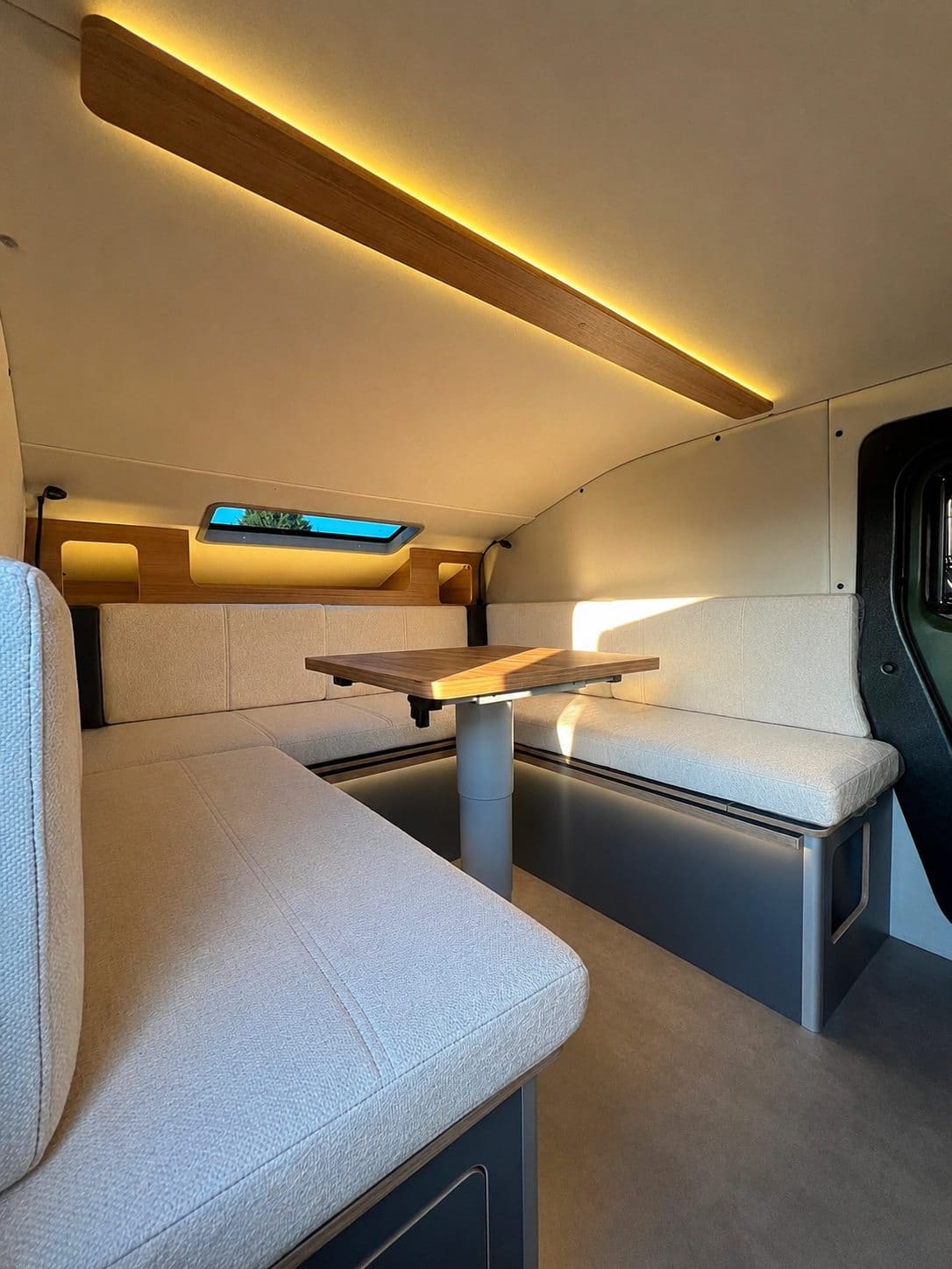 Bench seating around a wooden table on a single leg inside the Urban Badger Towable Caravan, with an LED strip above