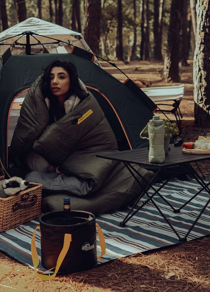 Woman in a sleeping bag on the striped Wunjo picnic blanket next to the Midgard tent